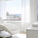 ¿Se puede hacer un injerto capilar con lupus? Sala de valoración premium en Clínica Frontela Huelva con escultura de mariposa cristal simbolizando conciencia del lupus sobre toalla blanca para la evaluación capilar de pacientes con lupus