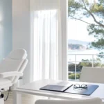 ¿Cuándo se puede volver al trabajo después de un injerto capilar? Sala de valoración premium en Clínica Frontela Huelva con carpeta de cuero y gafas sobre escritorio blanco para planificar la reincorporación laboral tras el trasplante capilar